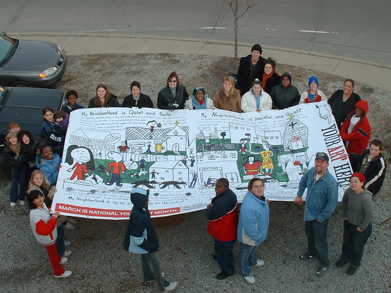 Billboard Generation II, 2004. The second Youth Art billboard competition took place in Bloomington and Indianapolis, resulting in four billboards in each city. Eight different artworks made by students in grades k-12 responded to the question "What would you like to tell your community?" Winning themes included the effects of pollution on our environment, diversity, and the importance of community involvement. Members of Your Art Here hanging "My Neighborhood Is, Billboard Generation II, Indianapolis, IN, 2004" with winnners from the Minnie Hartman School, Indianapolis thumbnail-2